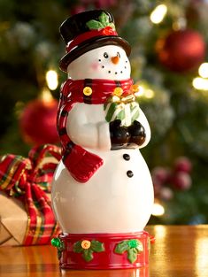 a snowman figurine sitting on top of a table next to a christmas tree