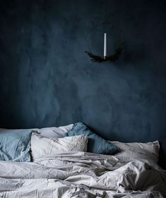 an unmade bed with white sheets and blue walls