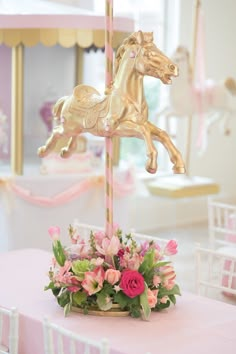 a pink and gold carousel with flowers on the table in front of it is also a rocking horse