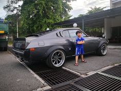 a young boy standing next to a gray car