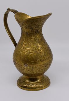 an antique brass pitcher with floral designs on the handle and sides, sitting on a white background