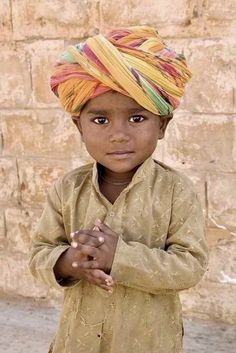 a young boy wearing a turban and standing in front of a stone wall