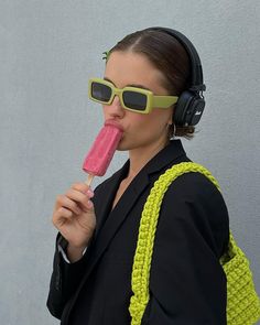 a woman wearing headphones and sunglasses is eating an ice - cream popsicle in front of her face