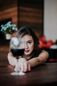 a woman is sitting at a table with a glass of red wine in her hand