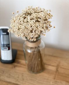 a glass vase filled with dried flowers next to an old cell phone on a wooden table