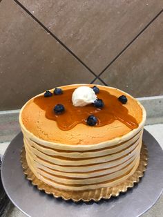 a stack of pancakes covered in syrup and blueberries on a metal platter next to a wall