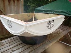 a white boat sitting on top of a wooden bench next to a green umbrella and some trees