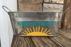 a metal bucket with the word sunscreen painted on it sitting on a wooden table