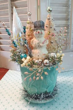 a snowman sitting in a blue cup filled with christmas decorations and other holiday items