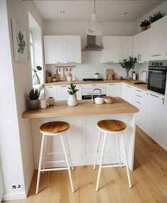 two stools are sitting at the counter in this white and wood themed home kitchen