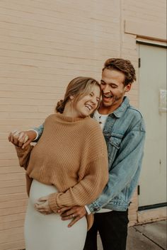 a man and woman standing next to each other in front of a brick building smiling