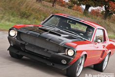 a red and black muscle car driving down the road