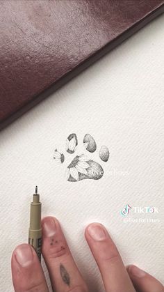 a hand holding an ink pen and drawing a paw print on a piece of paper