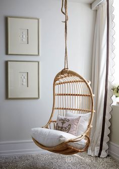 a hanging chair in the corner of a room with white walls and pillows on it