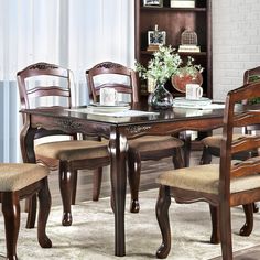 a dining room table with chairs and a bookcase in the corner next to it