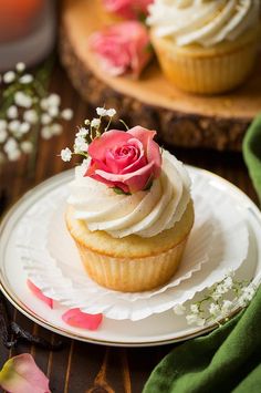 two cupcakes with white frosting and pink roses on top sitting on a plate