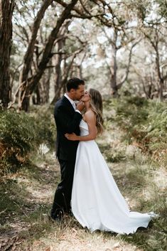 a bride and groom kissing in the woods