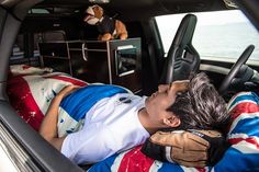 a man sleeping in the back seat of a car with stuffed animals on the dashboard