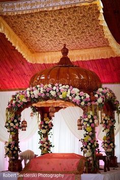 a bed with flowers on it under a canopy in the middle of a room filled with white drapes