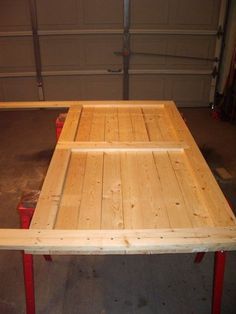 a table made out of wood and red metal legs in a garage with a garage door behind it