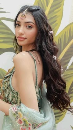 a woman with long dark hair wearing a green dress and flower in her hair, posing for the camera