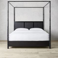 a four poster bed with white sheets and black headboard, against a gray wall