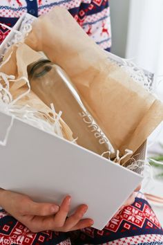 a person holding a box with a bottle in it and wrapping paper around the bottom