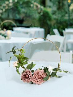 two pink roses in a basket on top of a table with white linens and greenery