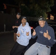 three young men standing next to each other in front of a car giving thumbs up