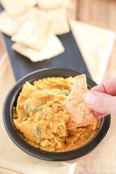 a hand holding a cracker over a bowl of hummus