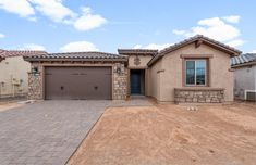 a house that is in the middle of a dirt lot with a brick driveway and two garages