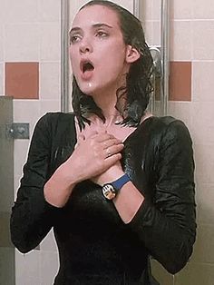 a woman standing in front of a shower with her hands on her chest and mouth open