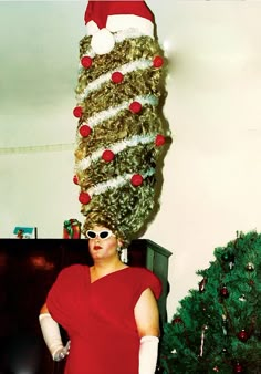 a woman in red dress standing next to a christmas tree with fake hair on it