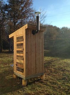 a small wooden outhouse sitting in the middle of a field with a pipe sticking out of it's roof