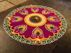 a colorful rangdi design on the ground with a lit candle in front of it