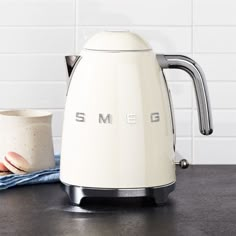 an electric kettle with the word smeg on it next to a mug and napkin