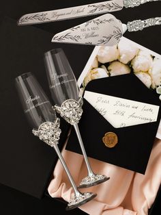 two champagne flutes sitting on top of a table next to an envelope and some flowers