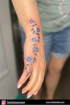 a woman's hand with blue flowers and leaves tattooed on the left side of her arm