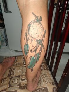 a man's leg with a tattoo on it that has a dream catcher and arrows