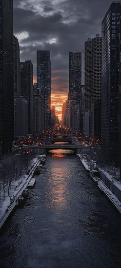 the sun is setting over a river with snow on the ground and buildings in the background