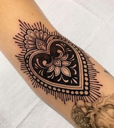 a black and white heart tattoo on the right arm, with an ornate border around it