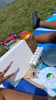 a woman sitting on top of a blue blanket next to a body of water holding a paintbrush