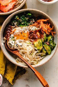 two bowls filled with different types of food on top of a white tablecloth and wooden spoons