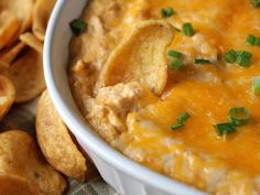 a white bowl filled with cheese dip and tortilla chips on a table next to some crackers