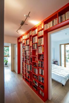 a red book shelf filled with lots of books next to a bed in a room