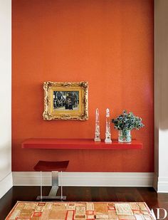 an orange room with a painting on the wall and vases in front of it