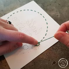 two hands are stitching the word love on a piece of white paper with green thread