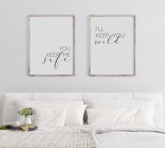 two framed art prints on the wall above a bed in a white room with pillows and blankets