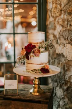 a three tiered wedding cake with red flowers on top sits in front of a window