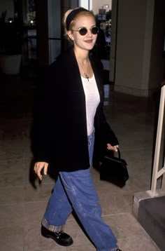 a woman in black jacket and jeans walking through an airport with her hand on her hip